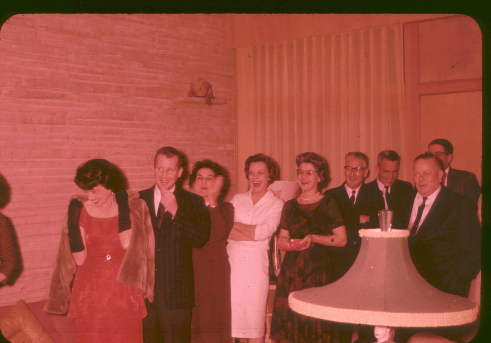 A Christmas gathering in the 1960s — the family laughing together against a white brick wall, the women in evening dresses, the men in dark suits.