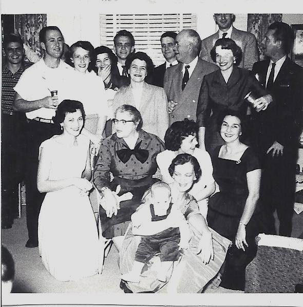 A crowded living room at Christmas in the 1950s — three rows of family, the men standing at the back, a toddler on his mother's lap at the front.