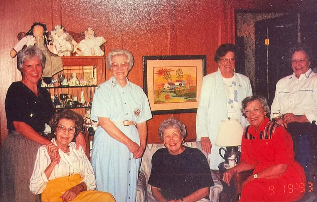 Seven women of the family gathered in a wood-panelled living room in 1993 — Aunt Mabel standing in a pale blue dress, Rob's grandmother seated at the right in red.
